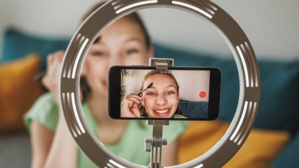 An image of a female teen doing a beauty routine video stream, as shown on the screen of a smartphone 